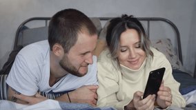 Couple using mobile phone to live stream, video call to friends in bed, weaving good bye. Caucasian man and woman.