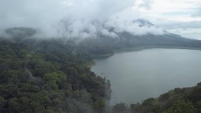 Aerial wide view of foggy mountain, tropical forest and lake. The drone flies in the clouds over a lake and jungle, around top of the mountains, 4k