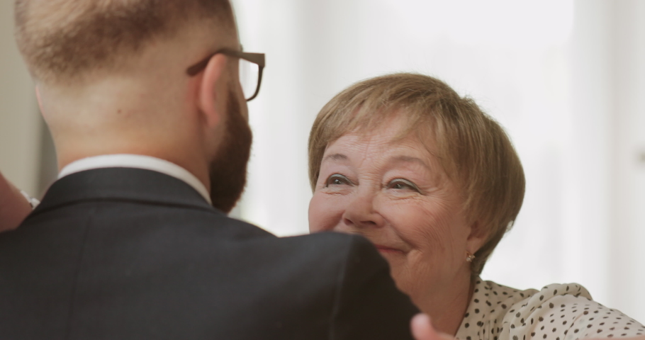 Close up view of smiling mature mother hugging her adult son while holding flowers in her hand. Man visiting his elderly mother at home. Concept of family, mothers day and birthday Royalty-Free Stock Footage #1051440469