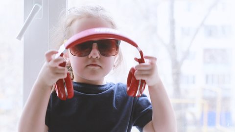 A close-up portrait of a little girl singing in sunglasses and headphones. Space for text