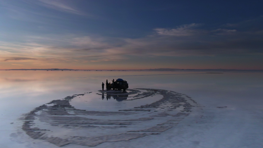 Uyuni Salt Flats (Spanish: Salar de Uyuni) in Bolivia, aerial view with drone orbiting group of tourists exploring the salt flats at sunrise. 