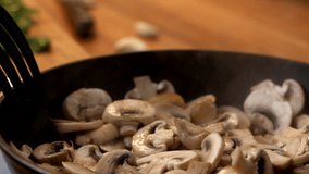 Close-up of woman with wooden spatula interferes with chopped champignon mushrooms in pan. Slow motion video
