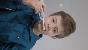 Young Teenager, school boy brushes teeth with an electric brush. He is bored. Vertical footages