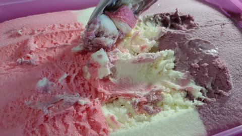 Strawberry, vanilla and black current flavored barbie theme striped ice cream in pink tub, delicious sunday dessert being scooped with stainless steel spoon.