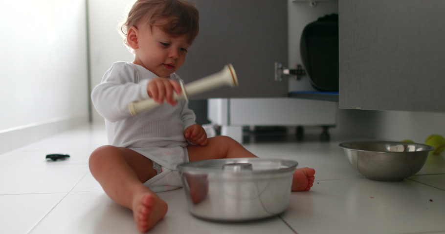 Baby playing with pans and pots on kitchen floor. One year old toddler infant hitting metal utensil