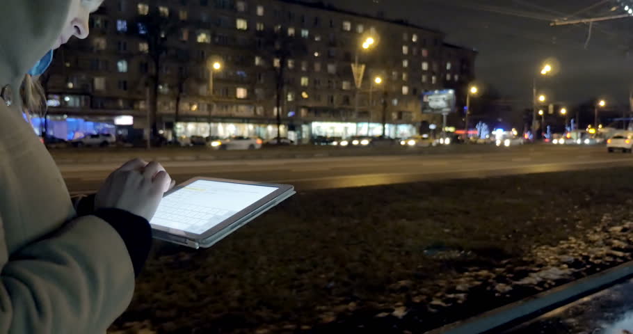 Steadicam shot of a woman with pad walking along the busy street in the eveing city  