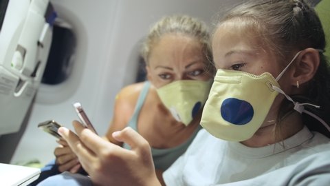 Family woman and child baby travel tourist caucasian at plane aircraft with wearing protective medical mask. Use smartphone mobile. Health virus protect coronavirus epidemic sars-cov-2 covid-19.