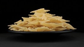 Farfalle pasta grains of spin around themselves on a black background and ground