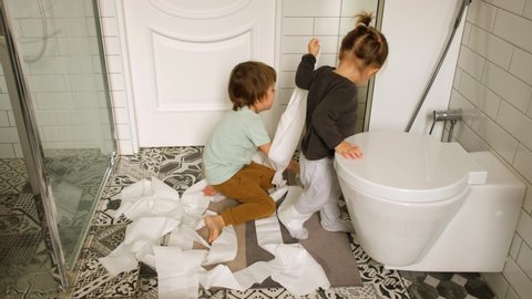 From above brother and sister throwing toilet paper on floor while playing in bathroom at home together