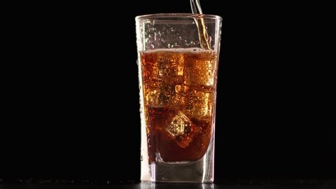 Amazing fresh coke with bubbles in transparent glassware isolated at black background. Pouring cola to beautiful goblet with crystal ice slow motion. 4k Dragon RED camera