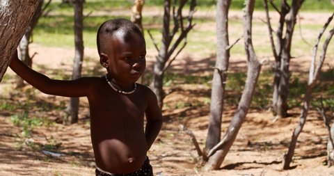 Child of Himba is standing and leaning on a tree, 25.01.2020, Kunene, Namibia