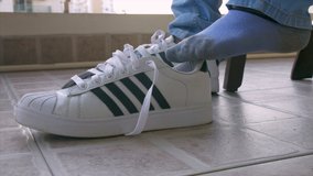 Close-up portrait of a man wearing casual shoes and tying up laces. HD Stock clip of a man wearing white shoes getting ready to go party