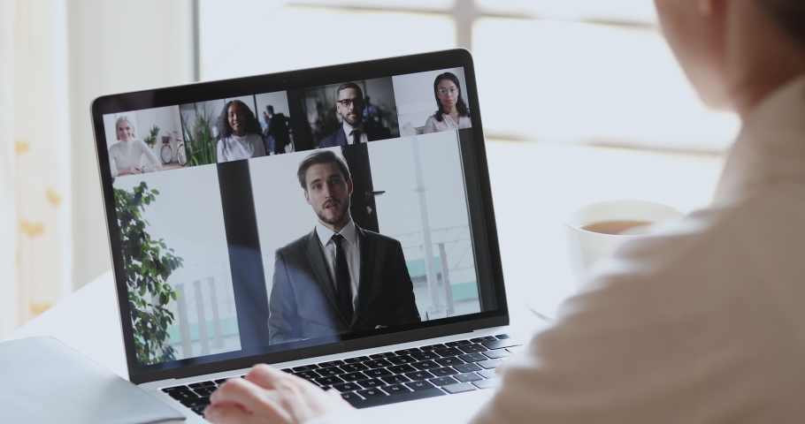 Male boss video conference calling corporate team people on laptop screen. Female distance employee talking with diverse colleagues group video conferencing in virtual webcam chat. Over shoulder view Royalty-Free Stock Footage #1051488610