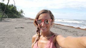 Young woman taking selfie on beach enjoying tropical climate video chatting online sharing adventures in Costa Rica