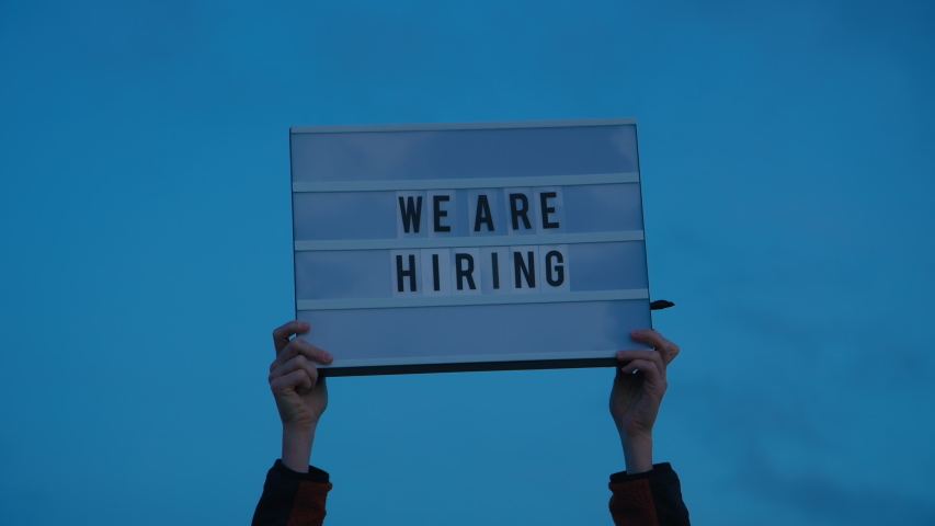 Hands hold up we are hiring sign on isolated sky background. Millennial or generation z hiring boom, surviving economical and financial crisis. Social media industry  Royalty-Free Stock Footage #1051500097