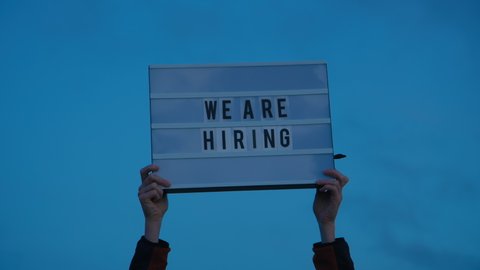 Hands hold up we are hiring sign on isolated sky background. Millennial or generation z hiring boom, surviving economical and financial crisis. Social media industry 