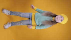 Cheerful cute little girl having fun and dancing on a yellow background. Studio shot. Vertical video