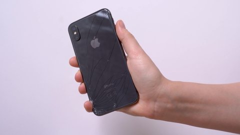 April 11, 2020, Rostov-on-Don, Russia: human hand holds smartphone iPhone X of space grey color with accidentally broken back glass, twists it and checks for damage and cracks with finger