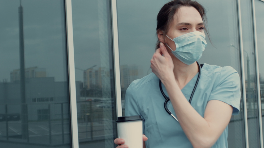 Portrait of tired exhausted nurse or doctor having a coffee break outside in the morning. COVID-19, Coronavirus pandemic. ARRI Alexa Mini Royalty-Free Stock Footage #1051515238