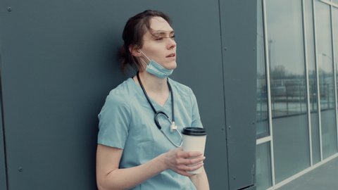 Portrait of tired exhausted nurse or doctor having a coffee break outside in the morning. COVID-19, Coronavirus pandemic. ARRI Alexa Mini