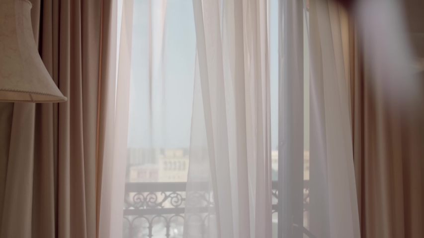 A woman in a white dress opening up the white curtains of the room and going to the balcony to enjoy the wonderful view of the city. Royalty-Free Stock Footage #1051518565