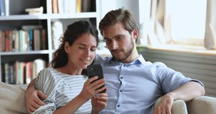 Overjoyed young couple looking at smart phone winning gift or prize in social media app sit on sofa at home. Excited happy millennial man and woman winners celebrating mobile victory together concept.