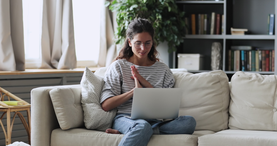 Happy young adult woman sitting in cozy living room on couch holding using laptop. Smiling casual lady chatting with friends, working or studying from home online on computer tech relaxing on sofa. Royalty-Free Stock Footage #1051518922