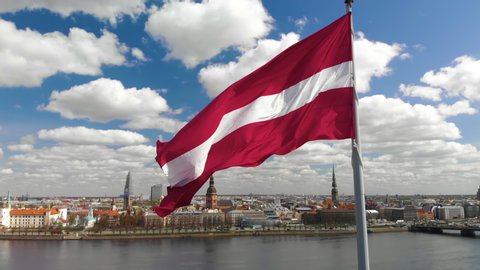 Huge latvian flag flutters on wind with Riga old town background