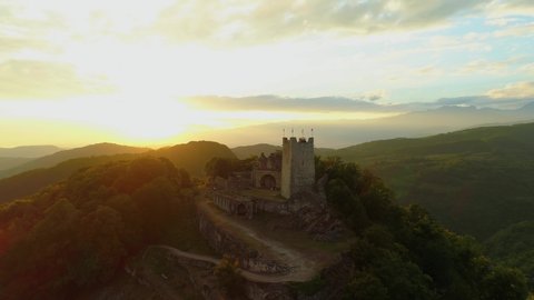 Beautiful orange sunset rays of sun Anacopia Fortress New Athos ancient stone stronghold on top of high mountain. Best natural landscape cityscape. Picturesque Abkhazia mountains horizon. Flight above