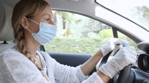 Young woman driving car wearing medical mask to prevent spreading COVID-19. Driving female with face mask and gloves in car to protect from the virus flu 