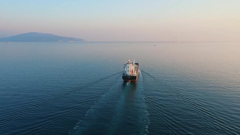 Aerial view following the ultra large cargo ship at sea leaves port at sunset. Top down drone footage of tanker. Concept of transport logistics, maritime.