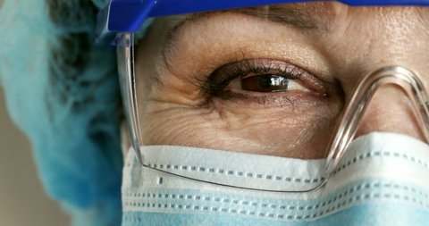 Close-up. Caucasian doctor woman with glasses and a medical mask smiles and nods her head approvingly. kind eyes of a doctor in a protective mask. COVID-19