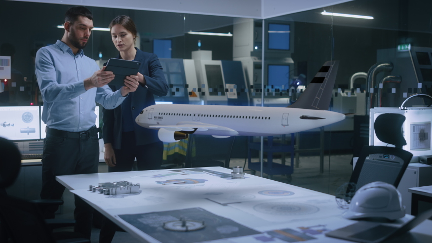 Aeronautics Factory Office Meeting Room: Engineer Holds Tablet Computer, Showing Augmented Reality Airplane Jet Engine to a Female Project Manager. Modern Industry 4.0 Research and Development Test.