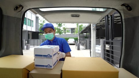 Corona Virus concept.Blue delivery handsome asian man wearing protection mask and medical rubber gloves puts cardboard boxes in the trunk of a car. Volunteer work in the midst of an epidemic. 