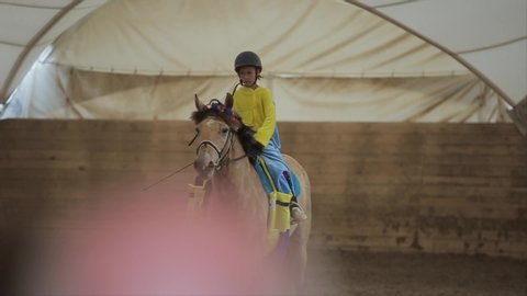 Minsk, Belarus - 19 July 2019: Little cute girl riding a horse in a minion costume at an indoor corral of a horse ranch