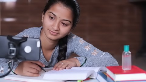 Selective focus of Mobile, Concept of e-learning at home due to covid-19 or coronavirus isolation - Young college girl taking notes by looking into virtual class on mobile due to isolation.