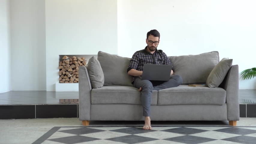 Young man typing on a laptop sitting on a couch. Working from home.