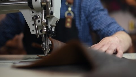 The craftsman sews a black strip on gray wallet with special sewing machine. White sewing machine needle and gray leather with seam. The leather craftsman produces leather products on sewing machine