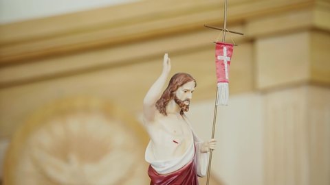 Figurine Jesus with his right hand raised up and a cross stands in a church, a holy bright place