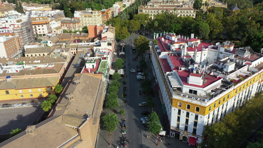 Aerial tilt down shot of people at tower by river and street in city, drone flying over famous landmark on sunny day - Seville, Spain