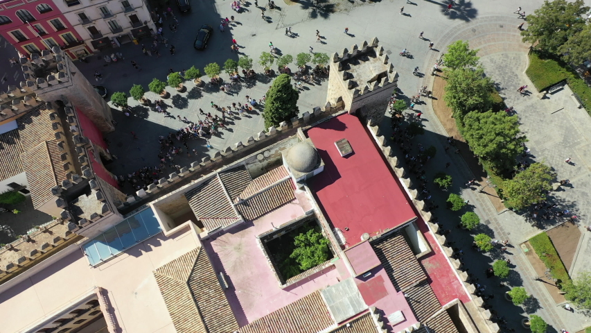 Aerial forward shot of people at Plaza del Triunfo amidst buildings, drone flying over tourists in city - Seville, Spain