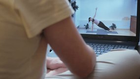 Girl yoga trainer conducts classes online to maintain health in quarantine. A man sits on a yoga mat at home, looks at self-isolation using a laptop.