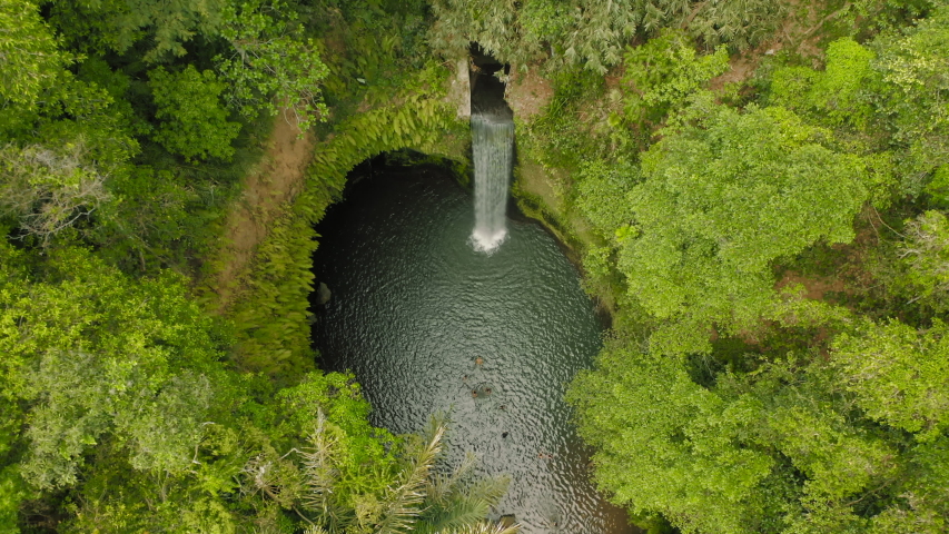 Aerial drone flight off fantastic cozy secret waterfall, Bali, Indonesia, 4k. Drone goes through green trees, palms and exotic plant to oasis hidden in the cave with high waterfall and small lake
