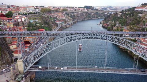Aerial tilt down shot of tourists on famous bridge over boat in river, drone flying over landmark amidst buildings in city - Porto, Portugal