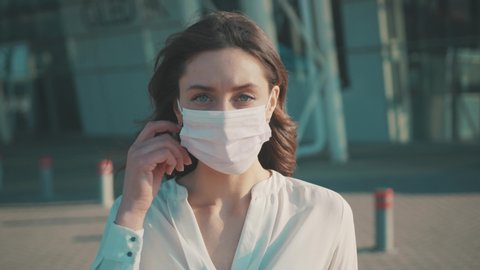 Pandemic Covid-19. Portrait nice brunette caucasian girl taking off medical mask looking serious outside at the airport. Health care, face protection. Quarantine.