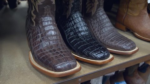 American-style boots from ostrich, crocodile and buffalo leather. Cowboy boots on a shelf in a store aligned, closeup. Side perspective close up on a pair of brown alligator leather cowboy boots.