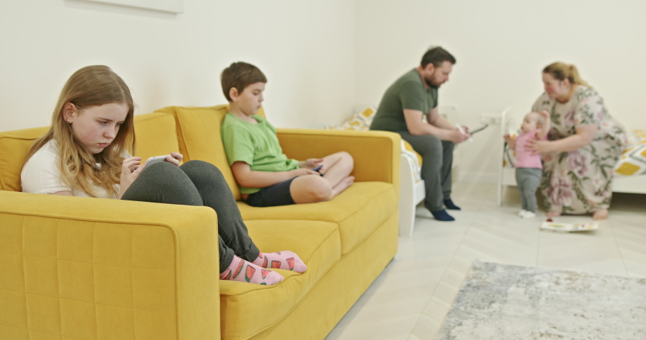 Siblings using smartphones near parents playing with baby