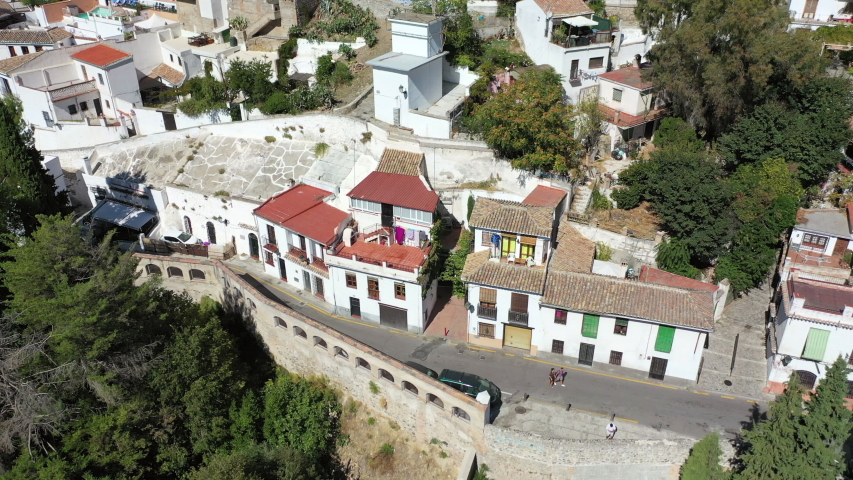 Aerial panning shot of tourists on street in city during sunny day, drone flying over residential buildings - Granada, Spain