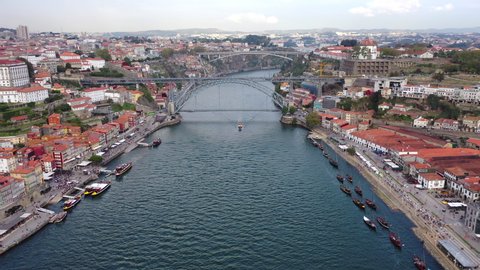 Aerial shot of vehicles on bridges over river with boats in city, drone flying forward amidst buildings against sky - Porto, Portugal