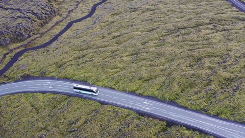 Aerial panning shot of bus on road amidst rocky landscape, drone flying over vehicle - Blue Lagoon, Iceland